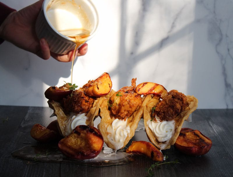 A hand pouring maple syrup over the three tacos